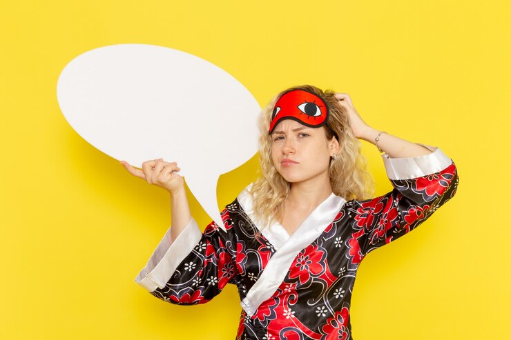 Foto grátis vista frontal jovem mulher com roupão segurando uma enorme placa branca na parede amarela cama noturna modelo menina cor
