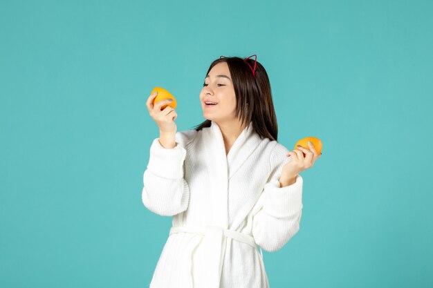 vista frontal jovem mulher em roupão segurando fatias de laranja em fundo azul