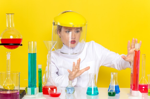 Foto grátis vista frontal, jovem química feminina em um terno branco com soluções de ed, trabalhando com eles, usando um capacete na ciência química espacial amarela.