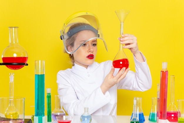 Vista frontal, jovem química feminina em um terno branco com soluções educacionais trabalhando com eles usando um capacete nos testes de química do espaço amarelo