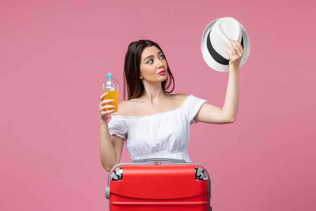 Vista frontal jovem segurando coquetel e chapéu de férias na parede rosa calor verão cor férias viagem viagem