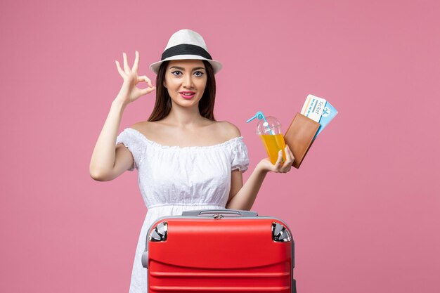 Vista frontal jovem segurando passagens de avião para as férias e suco na parede rosa verão emoção avião viagem