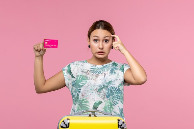 Vista frontal jovem segurando um cartão do banco de férias na parede rosa verão descanso viagem férias mulher