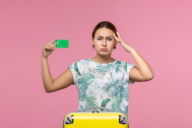 Vista frontal jovem segurando um cartão verde do banco de férias na parede rosa viagem férias viagem verão descanso mulher