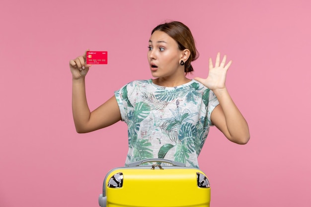 Vista frontal jovem segurando um cartão vermelho do banco em uma parede rosa claro voo mulher viagem aviões descanso de férias