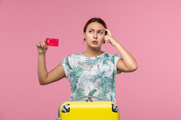 Vista frontal jovem segurando um cartão vermelho do banco na parede rosa voo mulher viagem avião férias descanso