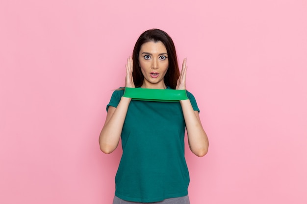 Vista frontal jovem segurando uma bandagem verde na parede rosa exercício esporte treino atleta cintura beleza