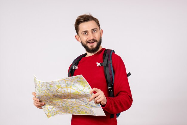 Vista frontal, jovem turista do sexo masculino com mochila explorando o mapa na parede branca plano covid avião férias emoções vírus voo cor