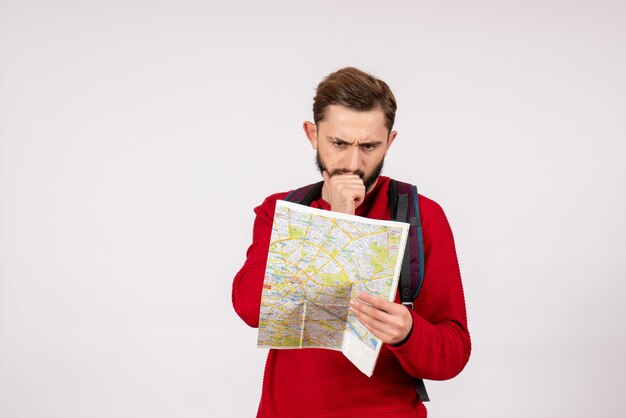 Vista frontal jovem turista masculino com mochila explorando o mapa na parede branca avião cidade férias emoção cor rota do turismo