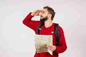 Foto grátis vista frontal jovem turista masculino com mochila explorando o mapa na parede branca avião cidade férias emoção humana rota de turismo