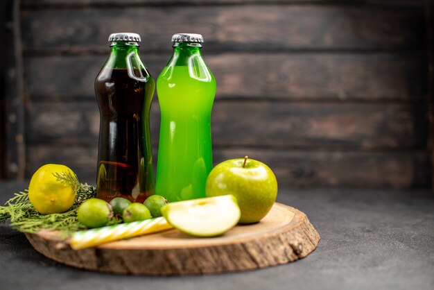 Vista frontal limonada verde preta em garrafas pipetas de feijoas de maçã e limão sobre placa de madeira