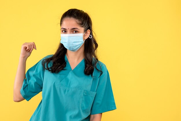 Vista frontal linda médica de uniforme apontando para trás em pé sobre fundo amarelo