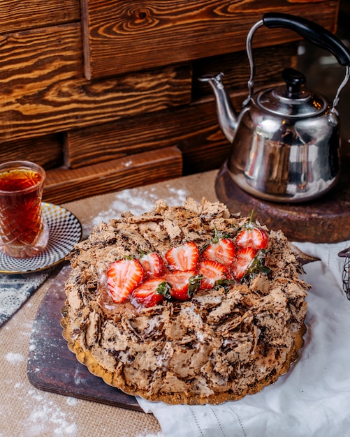 Vista frontal marrom bolo de chocolate com morangos frescos vermelhos por cima e chá quente no chão marrom