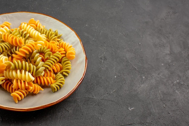 Vista frontal massa italiana cozida em espiral incomum dentro de um prato no espaço escuro