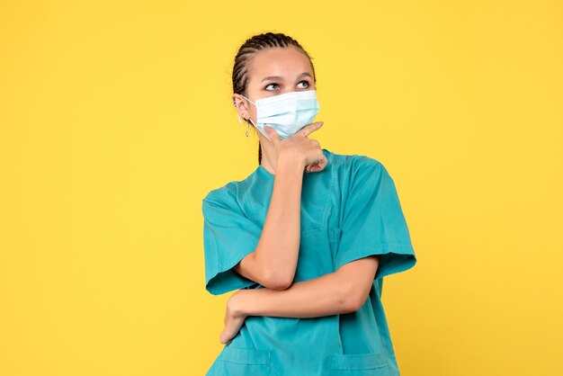 Vista frontal médica em camisa médica e máscara na secretária amarela. Enfermeira pandêmica vírus hospital saúde covid