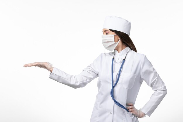 Vista frontal médica em traje médico branco com uma máscara devido à pandemia no vírus pandêmico de parede branca clara covid-