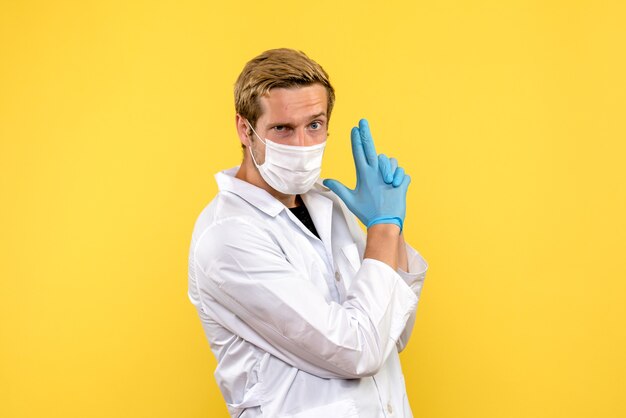 Vista frontal médico masculino segurando arma pose no fundo amarelo pandêmico médico saúde covid-