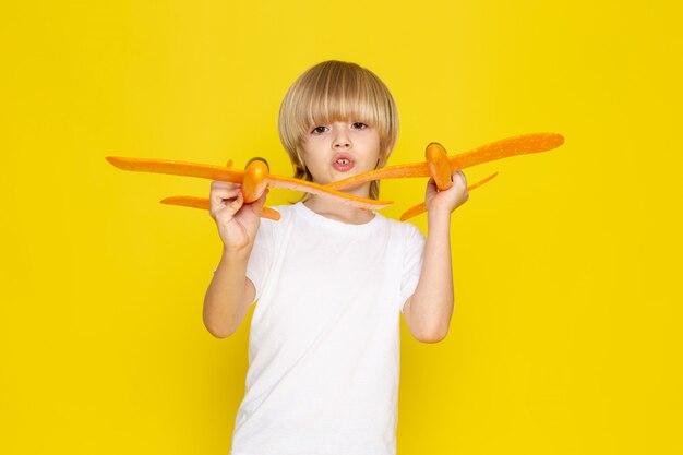 vista frontal menino loiro brincando com aviões de brinquedo laranja na camiseta branca amarelo