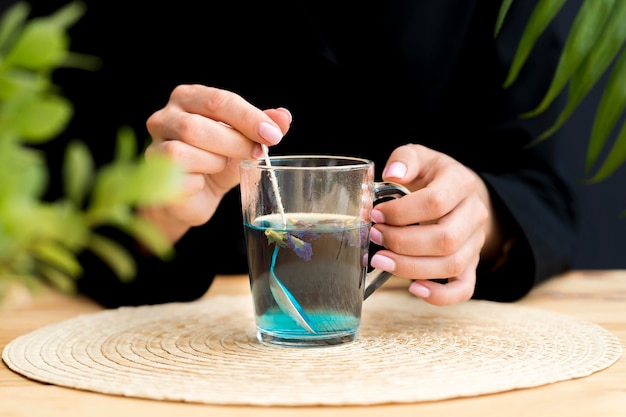 Vista frontal mulher mexendo chá azul em vidro