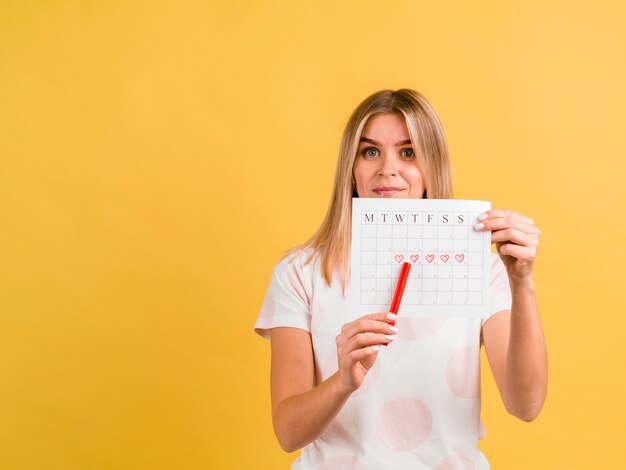 Vista frontal mulher mostrando seu calendário menstrual com uma caneta