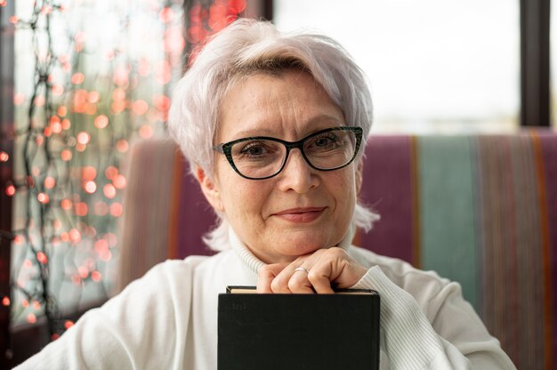 Vista frontal mulher sênior de óculos, segurando o livro