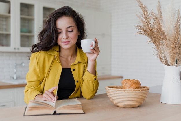 Vista frontal mulher sorridente com livro e xícara