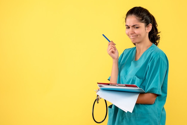 Foto grátis vista frontal pensando jovem médica verificando papéis em pé sobre fundo amarelo