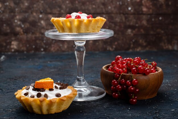 Vista frontal, pequenos bolos cremosos com cranberries vermelhas frescas na superfície escura doce