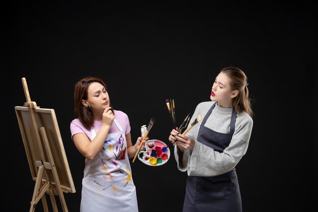 vista frontal pintora desenhando no cavalete com outra mulher na parede preta artista foto arte colorida imagem pintura desenho