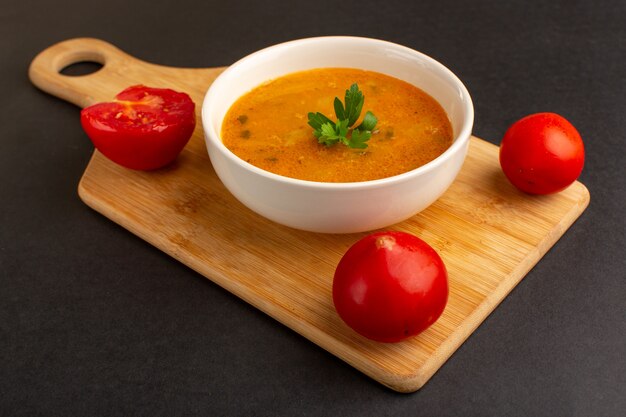 Vista frontal saborosa sopa de vegetais dentro do prato, juntamente com os tomates na mesa escura.