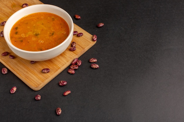 Foto grátis vista frontal saborosa sopa de vegetais dentro do prato junto com feijão cru na mesa escura.