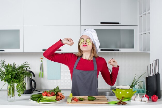 Vista frontal se espreguiçando, chef feminina de uniforme, colocando fatias de pepino no rosto