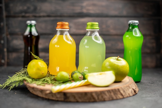 Vista frontal suco de frutas em garrafas de maçã limão feijoas pipetas em tábua de madeira limonadas em superfície escura