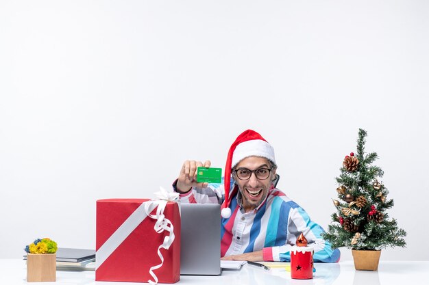 Vista frontal, trabalhador masculino, sentado em seu local de trabalho, segurando um cartão de banco verde, férias, emoção, natal, escritório, trabalho