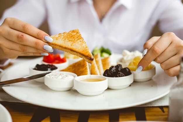 Vista frontal, uma mulher tem café da manhã torrada frita com geléia de creme de leite com manteiga de mel e azeitonas em um prato