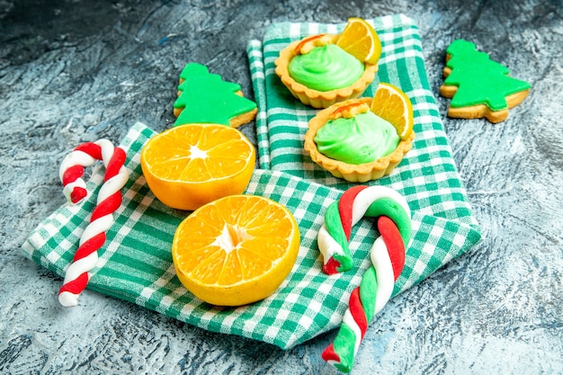 Vista inferior, corte laranjas doces da árvore de Natal pequenas tortas na toalha de cozinha quadriculada branca verde na mesa cinza