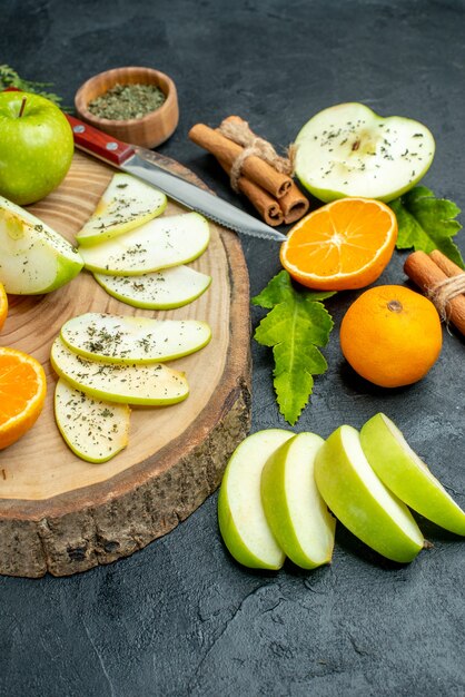 Vista inferior da faca de fatias de maçã e tangerinas na placa de madeira em bastões de canela amarrados com pó de menta seca por corda em fundo escuro