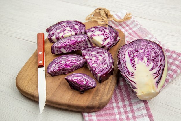 Vista inferior da faca de repolho roxo picado na placa de madeira na toalha de cozinha quadriculada rosa branca na mesa cinza