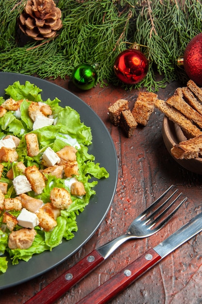 Vista inferior da salada Caesar em prato oval garfo e faca com crosta seca em mesa vermelha escura