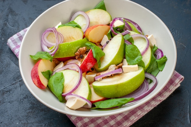 Vista inferior da salada de maçã em uma tigela, guardanapo xadrez branco rosa na mesa escura