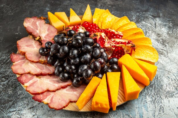 Vista inferior das fatias de carne, queijo, uvas e romã em uma mesa oval em fundo escuro