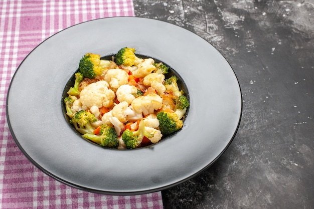 Vista inferior de brócolis e salada de couve-flor em um prato oval preto na bandeja de serviço. toalha de mesa quadriculada rosa e branca em fundo escuro