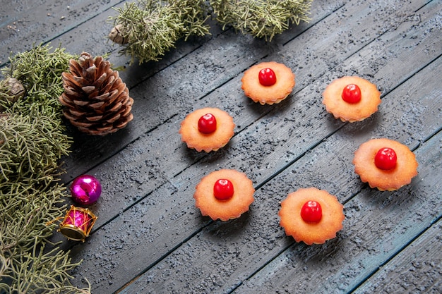 Vista inferior de cupcakes de cereja arredondados ramos de árvore de abeto, brinquedos de natal e um cone em solo escuro de madeira