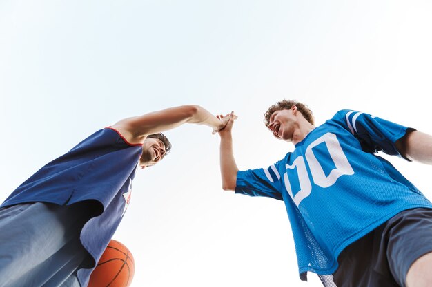 Vista inferior de dois jogadores de basquete confiantes e felizes em pé ao ar livre, batendo os punhos