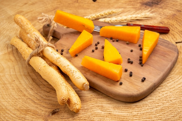 Vista inferior de fatias de queijo espalhado com pimenta do reino e garfo na tábua de trigo espiga pão na mesa de madeira