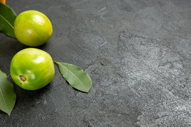 Vista inferior de folhas de louro com tomates verdes em fundo escuro