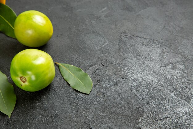 Vista inferior de folhas de louro com tomates verdes em fundo escuro