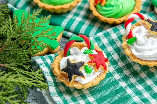 Vista inferior de pequenas tortas de natal em ramos de pinho na toalha de mesa na mesa cinza