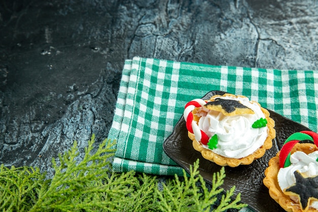 Vista inferior de pequenas tortas de natal em uma placa preta na toalha de mesa verde na mesa cinza