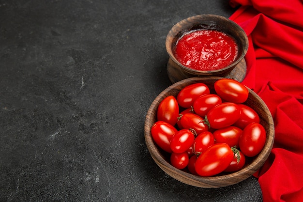 Vista inferior de tigelas com tomate cereja e toalha vermelha de ketchup em fundo escuro